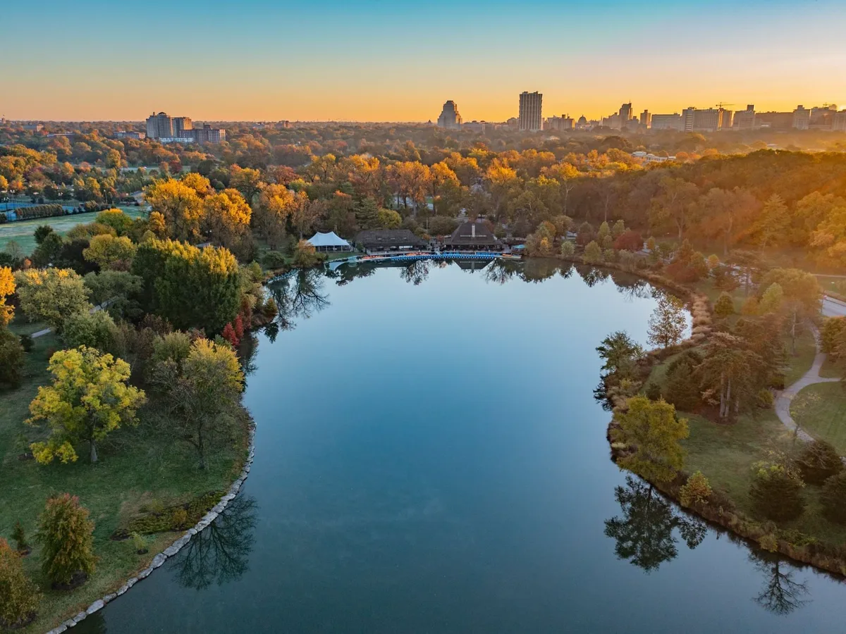 Aerial sunset view of a lake and wooded park in the St. Louis metro area, showing fall foliage and downtown skyline in the distance